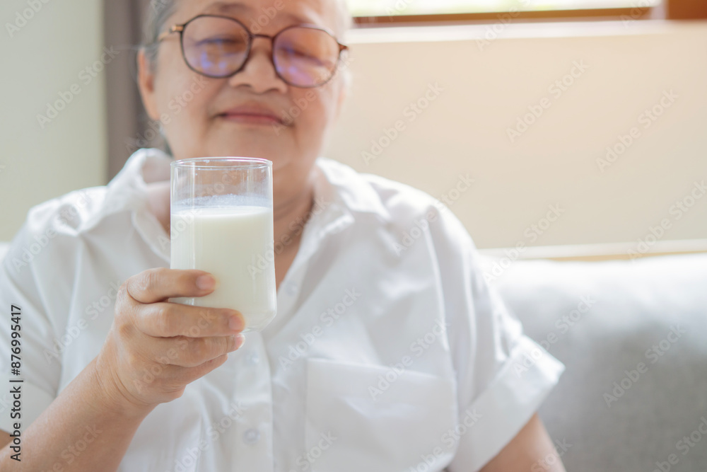 Senior Asian woman wearing eyeglasses drinking milk at home in the morning Senior Asian woman wearing eyeglasses drinking milk at home in the morning