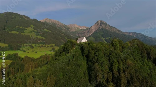 Schollanger burgkirche Fischen im Allgau, Bayern, Deutschland Luftaufnahme. Auwaldsee. Beautiful white church on top of mountain overlooking river, mountains and town of Fischen in Bavaria, Germany.  photo