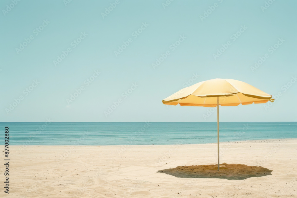 A lone yellow beach umbrella stands on an empty, sandy shore against a serene ocean backdrop A lone yellow beach umbrella stands on an empty, sandy shore against a serene ocean backdrop