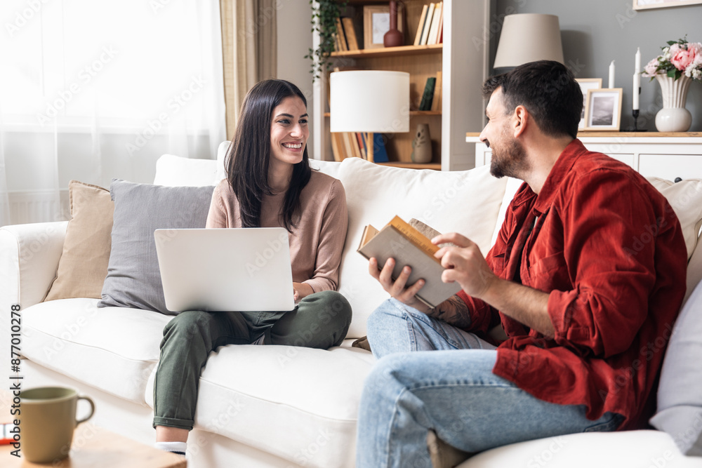 Simple living Young engaged couple sitting at home, spending quality time, woman searching for wedding dress on laptop, man reading a book, organizing wedding ceremony. Searching honeymoon destination Simple living Young engaged couple sitting at home, spending quality time, woman searching for wedding dress on laptop, man reading a book, organizing wedding ceremony. Searching honeymoon destination