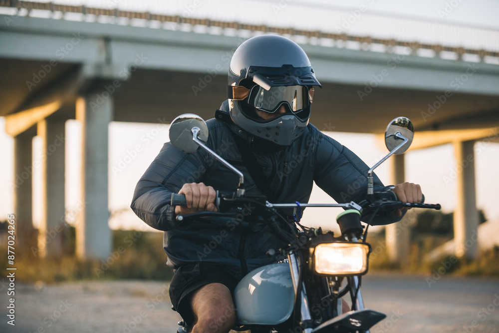 A young man in a helmet and goggles is enjoying his motorcycle on the road at sunset A young man in a helmet and goggles is enjoying his motorcycle on the road at sunset