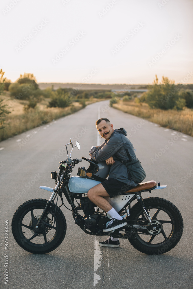 Obraz premium Biker on a cafe racer motorcycle on the road at sunset. Concept of riding a motorcycle at sunset.