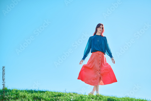 Wallpaper Mural Teenage girl in a blue blouse and orange skirt standing on grass against a clear blue sky. Outdoor fashion photography. Spring season concept. Torontodigital.ca