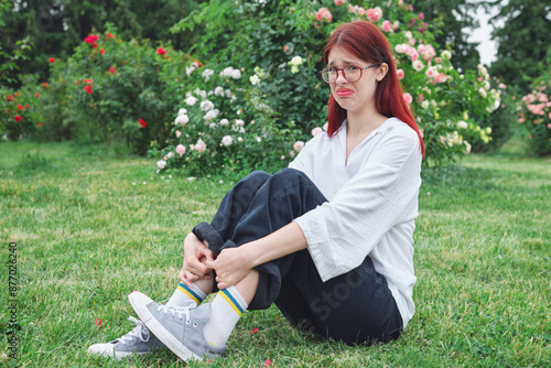 Canvas Print Teenage girl with red hair and glasses sitting in a blooming garden, making a di