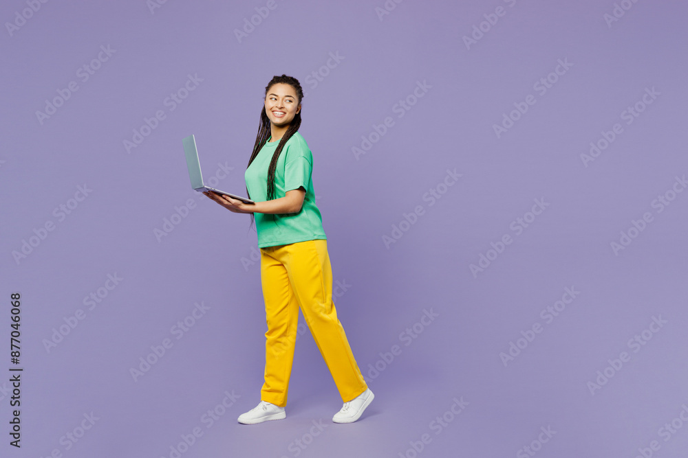 Full body young IT woman of African American ethnicity with dreadlocks wear t-shirt casual clothes hold use work on laptop pc computer look aside isolated on plain purple background Lifestyle concept Full body young IT woman of African American ethnicity with dreadlocks wear t-shirt casual clothes hold use work on laptop pc computer look aside isolated on plain purple background Lifestyle concept