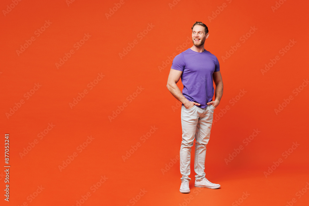 Full body young smiling happy cool man he wearing purple t-shirt casual clothes standing looking aside on area mock up copy space isolated on red orange background studio portrait. Lifestyle concept. Full body young smiling happy cool man he wearing purple t-shirt casual clothes standing looking aside on area mock up copy space isolated on red orange background studio portrait. Lifestyle concept.
