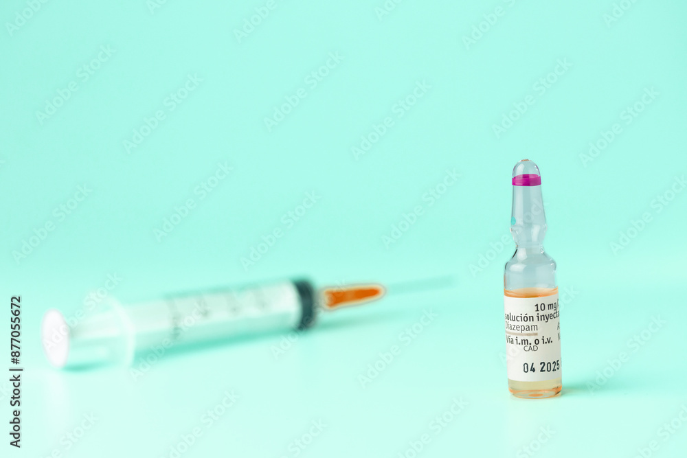A syringe and a small bottle of medicine are on a table. The syringe is attached to a needle and is filled with a clear liquid. The bottle is labeled with the name of the medicine A syringe and a small bottle of medicine are on a table. The syringe is attached to a needle and is filled with a clear liquid. The bottle is labeled with the name of the medicine