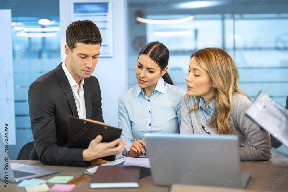 Business people in smart casual wear discussing documents and using a laptop while co-working in the office. Business people in smart casual wear discussing documents and using a laptop while co-working in the office.
