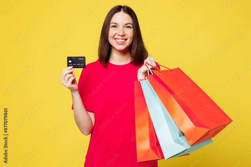 Young smiling woman wears pink casual clothes hold in hand paper package bags after shopping, show mock up of credit bank card isolated on plain yellow background. Black Friday sale buy day concept. Young smiling woman wears pink casual clothes hold in hand paper package bags after shopping, show mock up of credit bank card isolated on plain yellow background. Black Friday sale buy day concept.