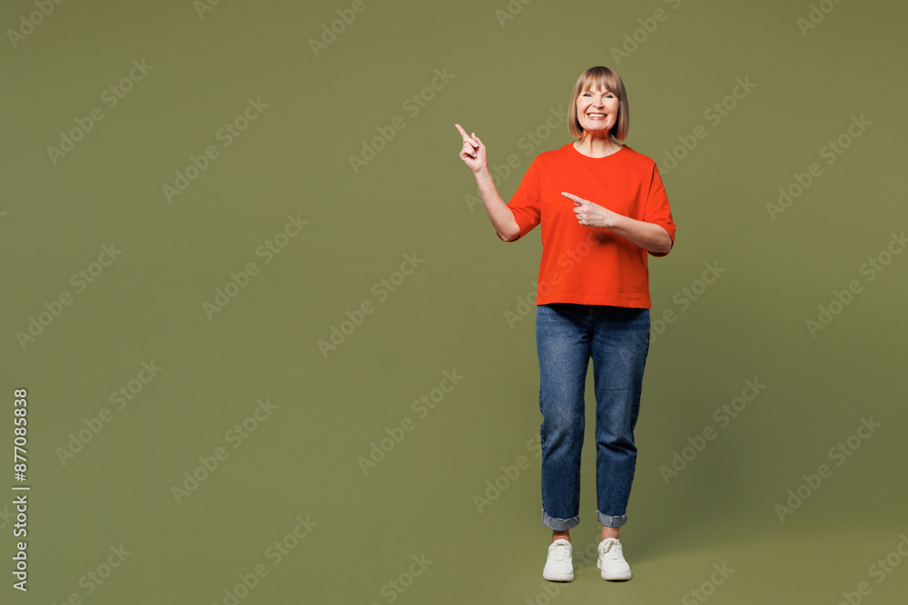 Φωτογραφία Full body smiling happy elderly blonde woman 50s years old she wear orange t-shirt casual clothes point index finger aside on area isolated on plain pastel green background studio