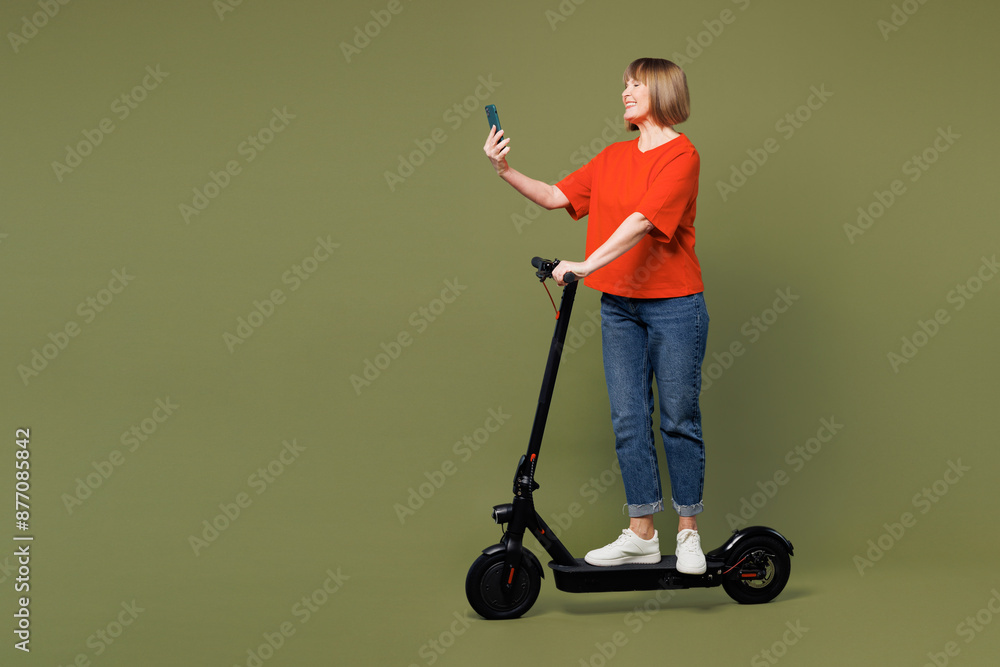 Φωτογραφία Full body side profile view elderly woman 50s years old wear orange t-shirt casual clothes riding electric scooter use mobile cell phone isolated on plain pastel green background