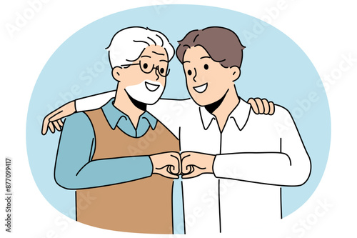 Young son and elderly father hug and bump fists to demonstrate unity and friendship between generations. Man of different ages say together we are strength, calling to be friends for generations
