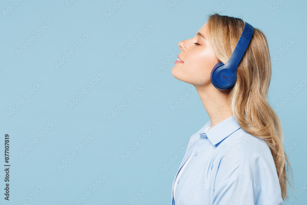 Side profile view young smiling happy woman wearing white top shirt casual clothes listen to music in headphones isolated on plain pastel light blue cyan background studio portrait. Lifestyle concept. Side profile view young smiling happy woman wearing white top shirt casual clothes listen to music in headphones isolated on plain pastel light blue cyan background studio portrait. Lifestyle concept.