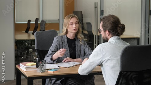 Two professional person having important meeting. A woman takes notes while listening attentively to her male colleague.