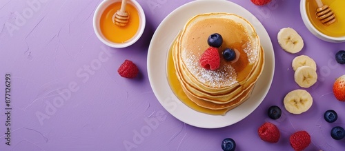 Top-down view of pancakes with honey and sweets presented on a purple backdrop with a blank area ideal for adding text or graphics - copy space image. photo