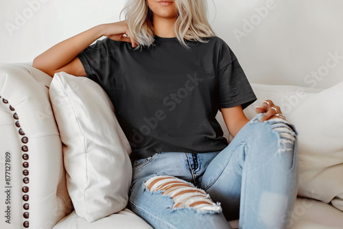 Blank black oversize t-shirt on a woman model sitting on the sofa. Minimalist Trendy t-shirt mockup.
