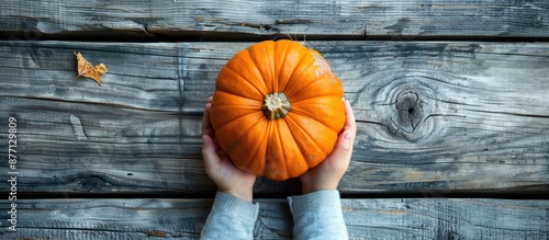 A pumpkin held by a child on a wooden board, viewed from above with space for text or images, symbolizing the autumn harvest season. photo