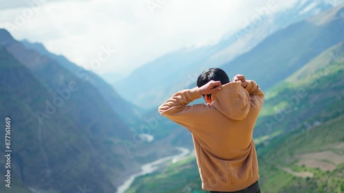 4K Rear view shot of a young Indian male tourist wearing hood of hoodie in front of the river flowing between two mountains at Tandi in Himachal Pradesh, India. Tourist covering his ears due to cold. photo