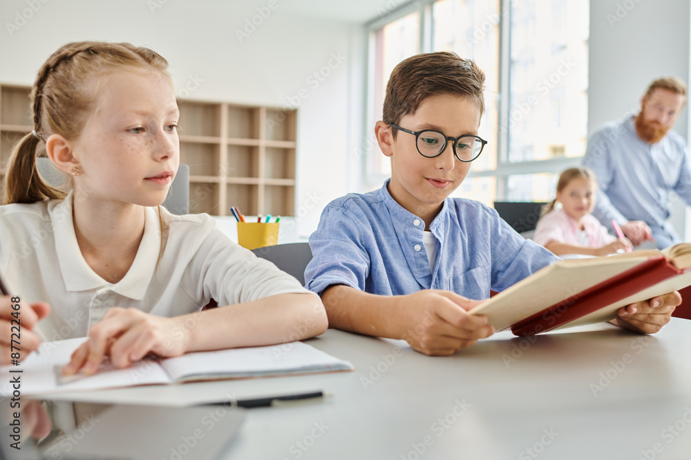 A boy and a girl sitting at a table, engrossed in reading a book together in a bright classroom setting. A boy and a girl sitting at a table, engrossed in reading a book together in a bright classroom setting.