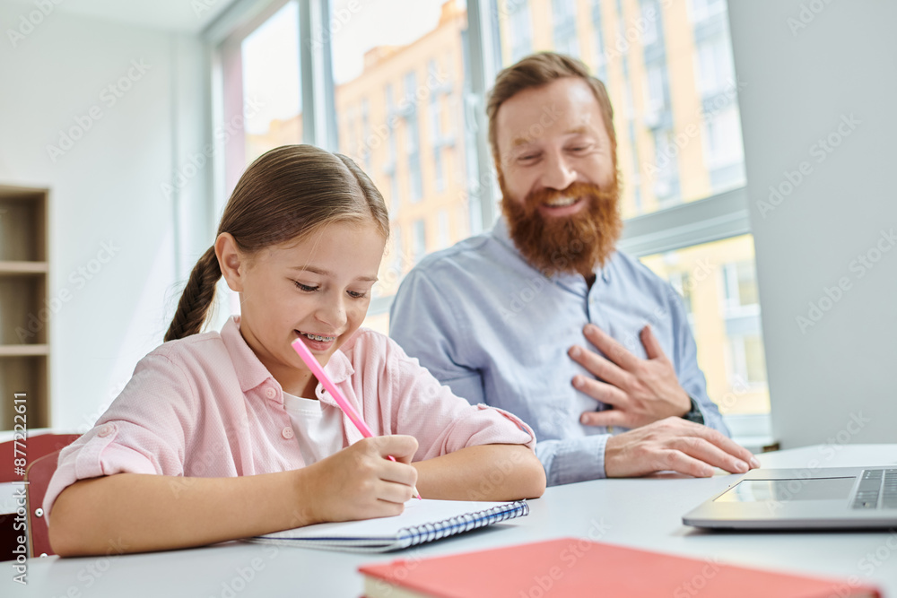 A man and a little girl engage in a lively lesson at a colorful table in a classroom setting. A man and a little girl engage in a lively lesson at a colorful table in a classroom setting.