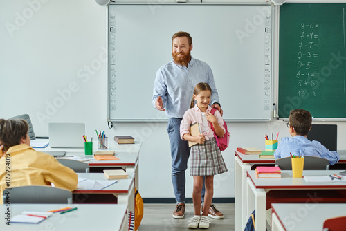 Canvas Print A man teacher stands beside a young girl in a vibrant classroom setting, engaging in interactive teaching
