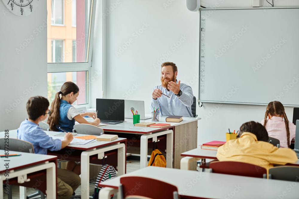 A male teacher sits before a group of students in a bright, lively classroom setting, engaging in interactive instruction.