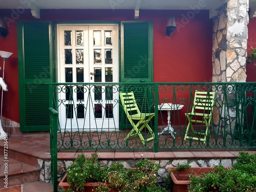 Green wooden door with a green wrought iron fence and two chairs on the terrace of a cafe