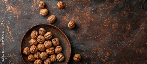 Top view of inshell walnuts arranged on a clay plate against a textured backdrop providing copy space image photo