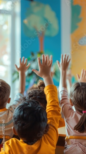 A group of children are raising their hands in a classroom. The children are wearing yellow shirts and are sitting at a table. Scene is one of learning and engagement