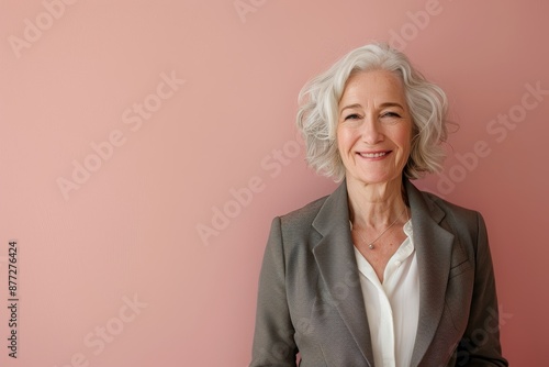 Portrait of a content caucasian woman in her 60s wearing a professional suit jacket in solid pastel color wall