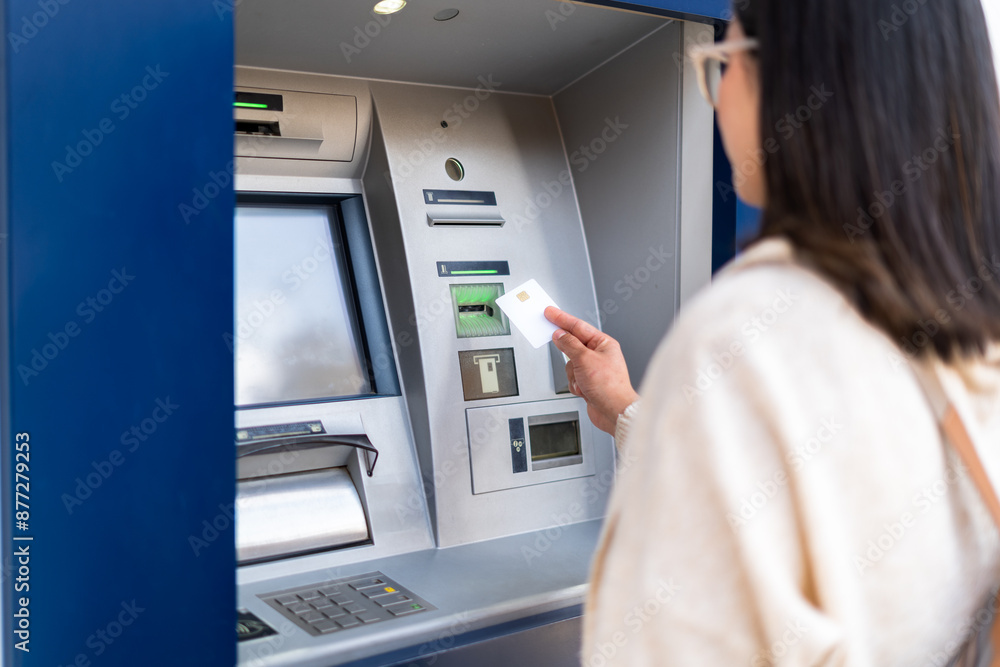 A woman uses an ATM machine, inserting her card for a transaction. The focus is on the card and machine. Finance and technology concept. A woman uses an ATM machine, inserting her card for a transaction. The focus is on the card and machine. Finance and technology concept.