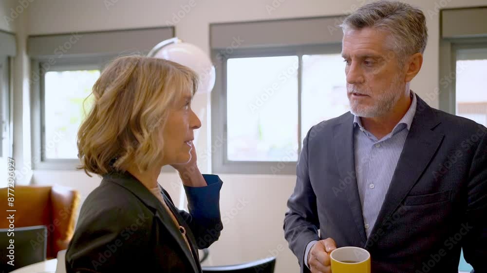 Business professionals engaging in a serious conversation in a modern office setting with natural light and coffee mug. Business professionals engaging in a serious conversation in a modern office setting with natural light and coffee mug.