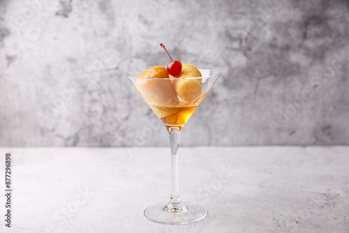 Neapolitan Rum baba (or baba au rum) in a martini glass with a cocktail cherry on a gray background. Small yeast cakes soaked in rum syrup. Traditional Italian pastry. Close-up, selective focus. photo