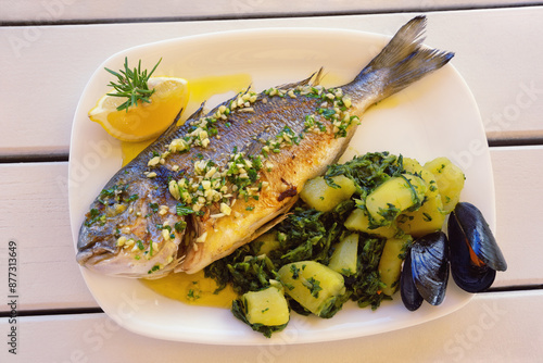 Balkan cuisine. Grilled fish ( sea bream ) with green leafy vegetables on white rustic table photo