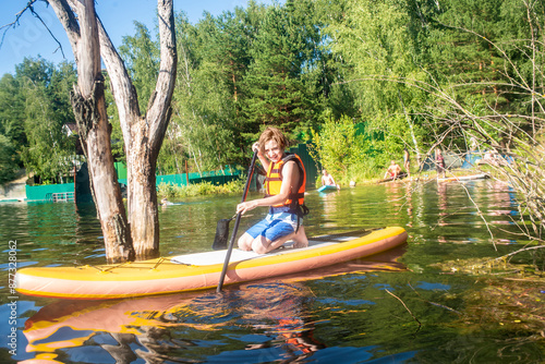 11 year old boy on a SUP board sitting on his knees, on a  lake in summer photo