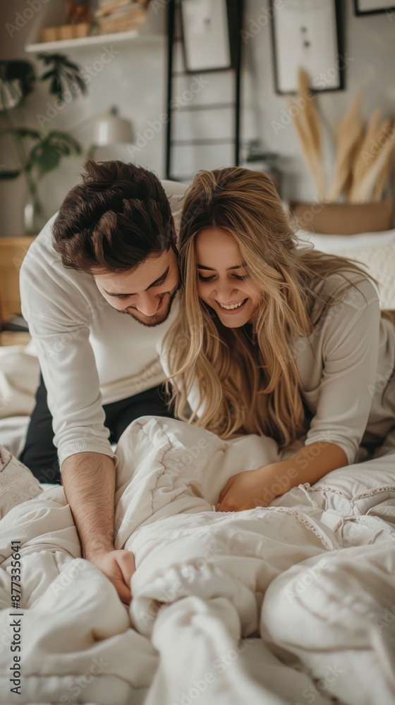 A couple playfully arranges a white blanket on a bed A couple playfully arranges a white blanket on a bed