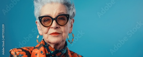Stylish senior woman in colorful attire and sunglasses against an blue background. Free copy space for banner.