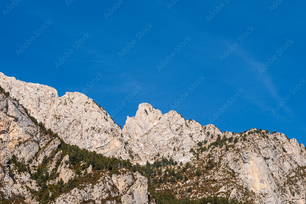 A stunning view of rugged mountain peaks under a bright blue sky with minimal clouds, displaying a mix of rocky formations and some greenery on the lower slopes. A stunning view of rugged mountain peaks under a bright blue sky with minimal clouds, displaying a mix of rocky formations and some greenery on the lower slopes.