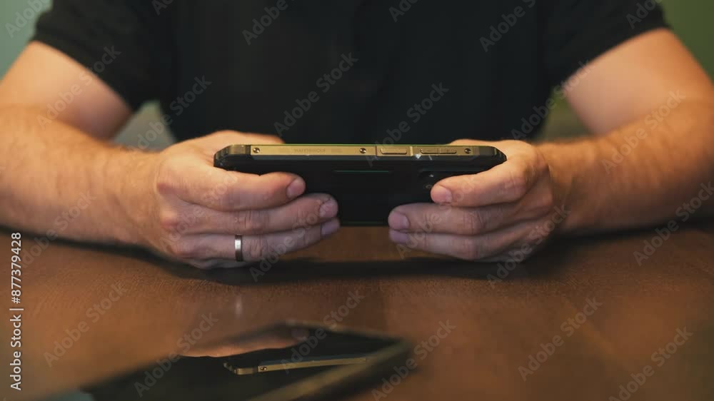 Closeup of focused man playing video game on phone. Gamer streaming games use mobile phone. Close up of adult male hands playing videogames on cellphone. Guy gaming on a smartphone at table desk Closeup of focused man playing video game on phone. Gamer streaming games use mobile phone. Close up of adult male hands playing videogames on cellphone. Guy gaming on a smartphone at table desk