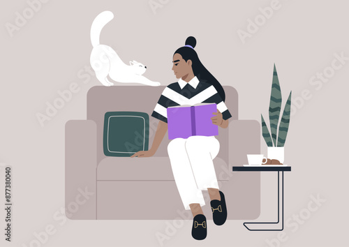 A woman relaxes on a couch, engrossed in a book, while her white cat stretches on the back of the sofa