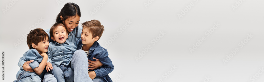 A group of children, including young Asian mother and her sons, playfully stack atop one another in a grey studio setting. A group of children, including young Asian mother and her sons, playfully stack atop one another in a grey studio setting.