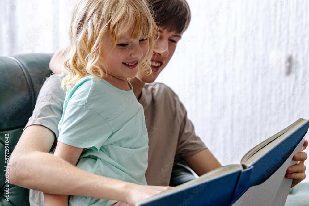 Smiling Boy Reading Book to Little Sister on Couch Smiling Boy Reading Book to Little Sister on Couch