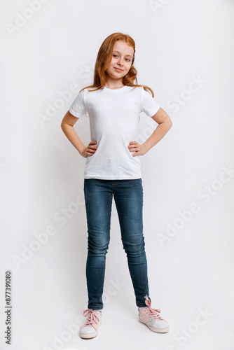 Redhead kid model in white t-shirt and jeans posing in studio. Full length portrait little girl