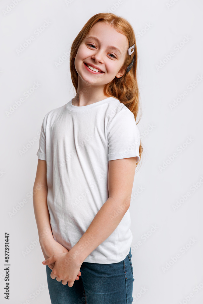 Smiling little redhead girl posing in blank white t-shirt with copy space on white studio background Smiling little redhead girl posing in blank white t-shirt with copy space on white studio background