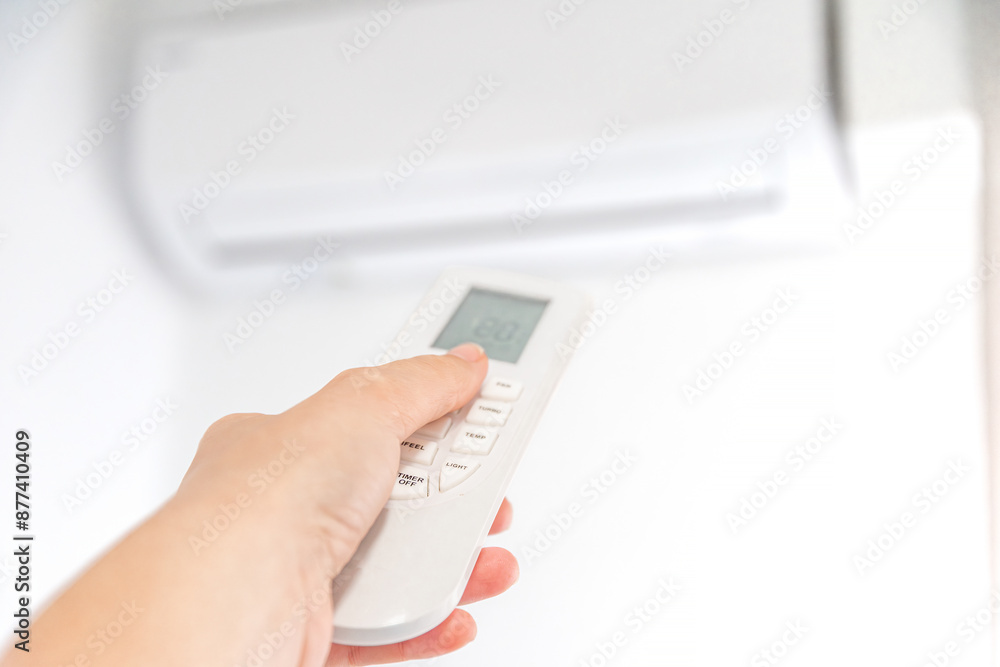 Fototapeta premium Hand Holding Remote Control Adjusting Air Conditioner