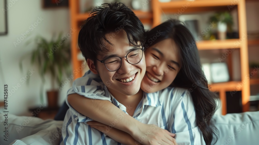 Happy couple embracing and smiling while sitting on a cozy sofa in a warm, well-decorated living room with a bookshelf in the background. Happy couple embracing and smiling while sitting on a cozy sofa in a warm, well-decorated living room with a bookshelf in the background.