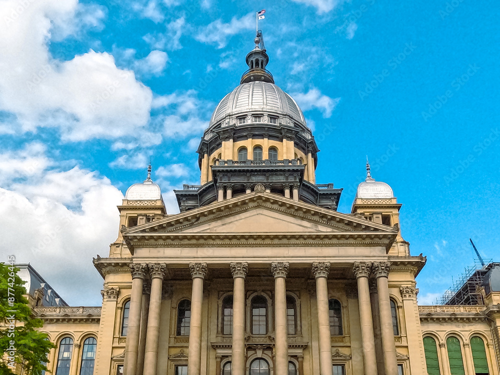 Front Views of the Illinois State Capitol Building in Springfield, IL, USA. Cloudy blue skies overhead. Scaffolding and construction equipment with ongoing construction on the building. Front Views of the Illinois State Capitol Building in Springfield, IL, USA. Cloudy blue skies overhead. Scaffolding and construction equipment with ongoing construction on the building.