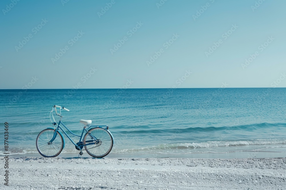 Fototapeta premium Blue bicycle is standing on a white sand beach with a turquoise sea and clear sky background, conveying a sense of freedom and adventure