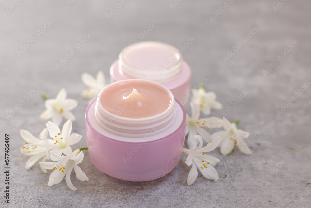 Cream in jars and beautiful jasmine flowers on grey table, closeup Cream in jars and beautiful jasmine flowers on grey table, closeup