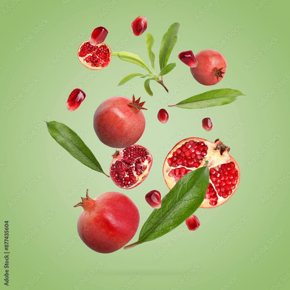 Fresh pomegranates, seeds and leaves in air on green background Fresh pomegranates, seeds and leaves in air on green background